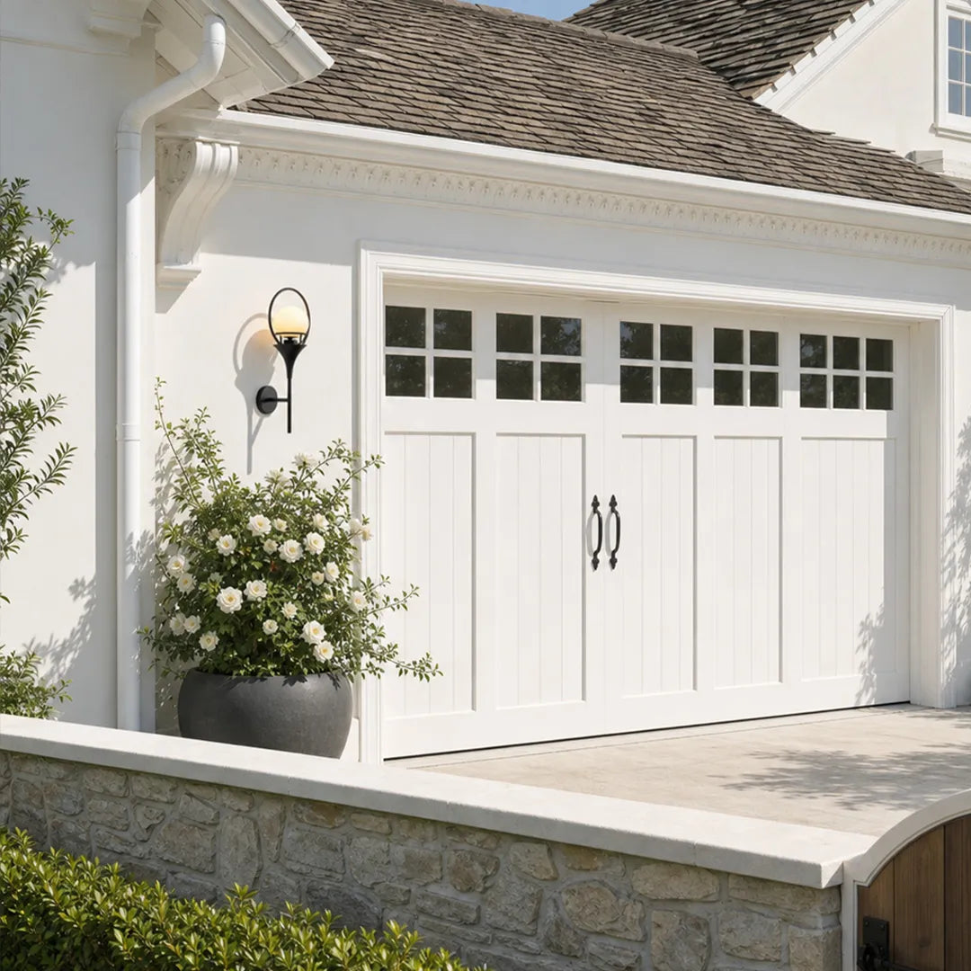 Wall mounted outdoor lighting installed beside a white garage door on a bright residential exterior.