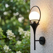 Wall mounted outdoor lighting with a black frame and glowing globe shade installed on a textured exterior wall.