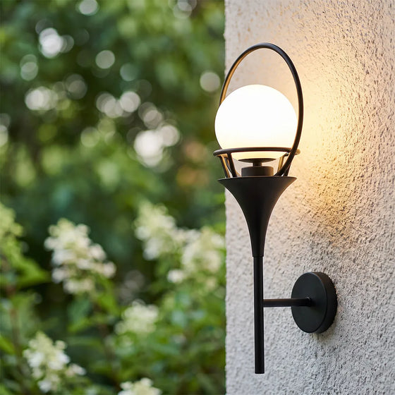 Wall mounted outdoor lighting with a black frame and glowing globe shade installed on a textured exterior wall.