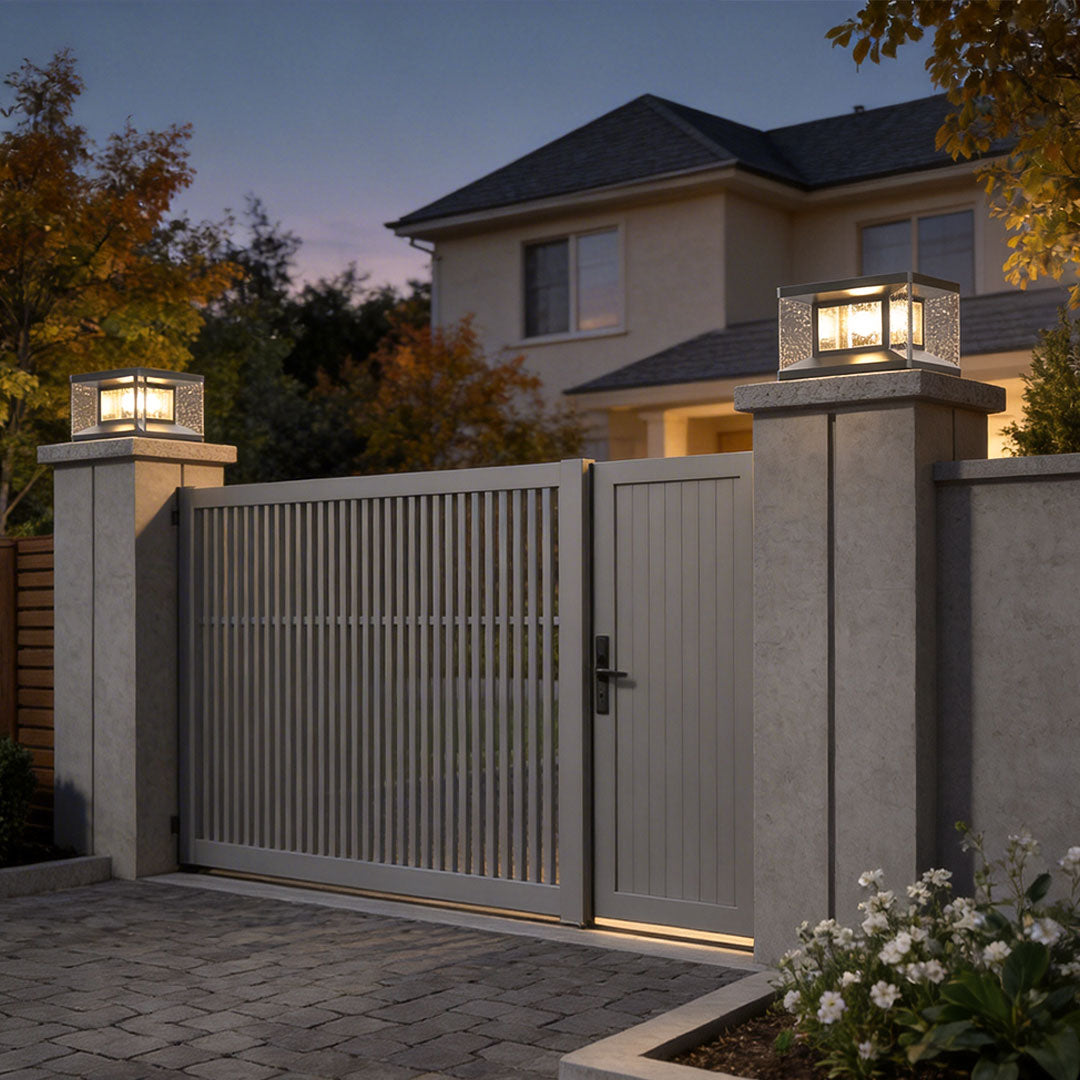 Wall pillar lights installed on stone pillars at the entrance of a modern house with a metal gate.