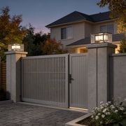 Wall pillar lights installed on stone pillars at the entrance of a modern house with a metal gate.