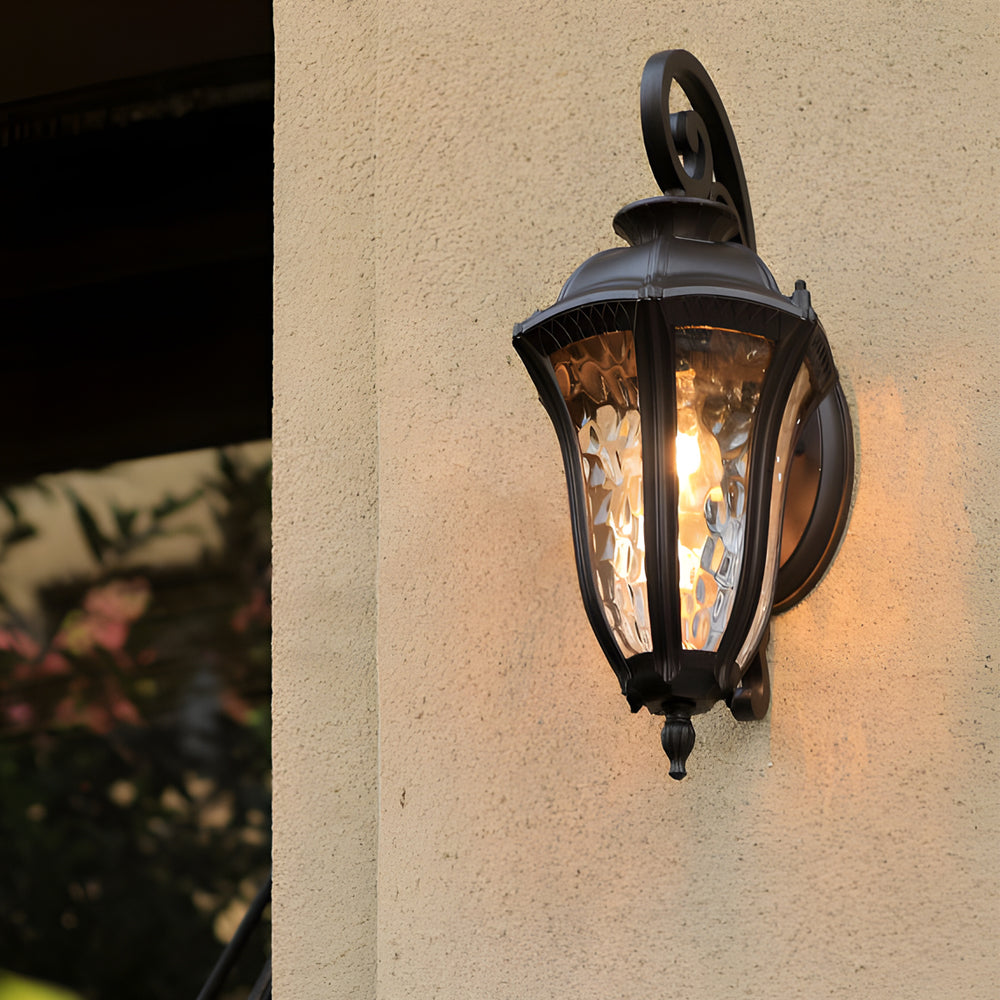 Wall sconce lantern with a black finish, casting a warm glow on a textured wall.