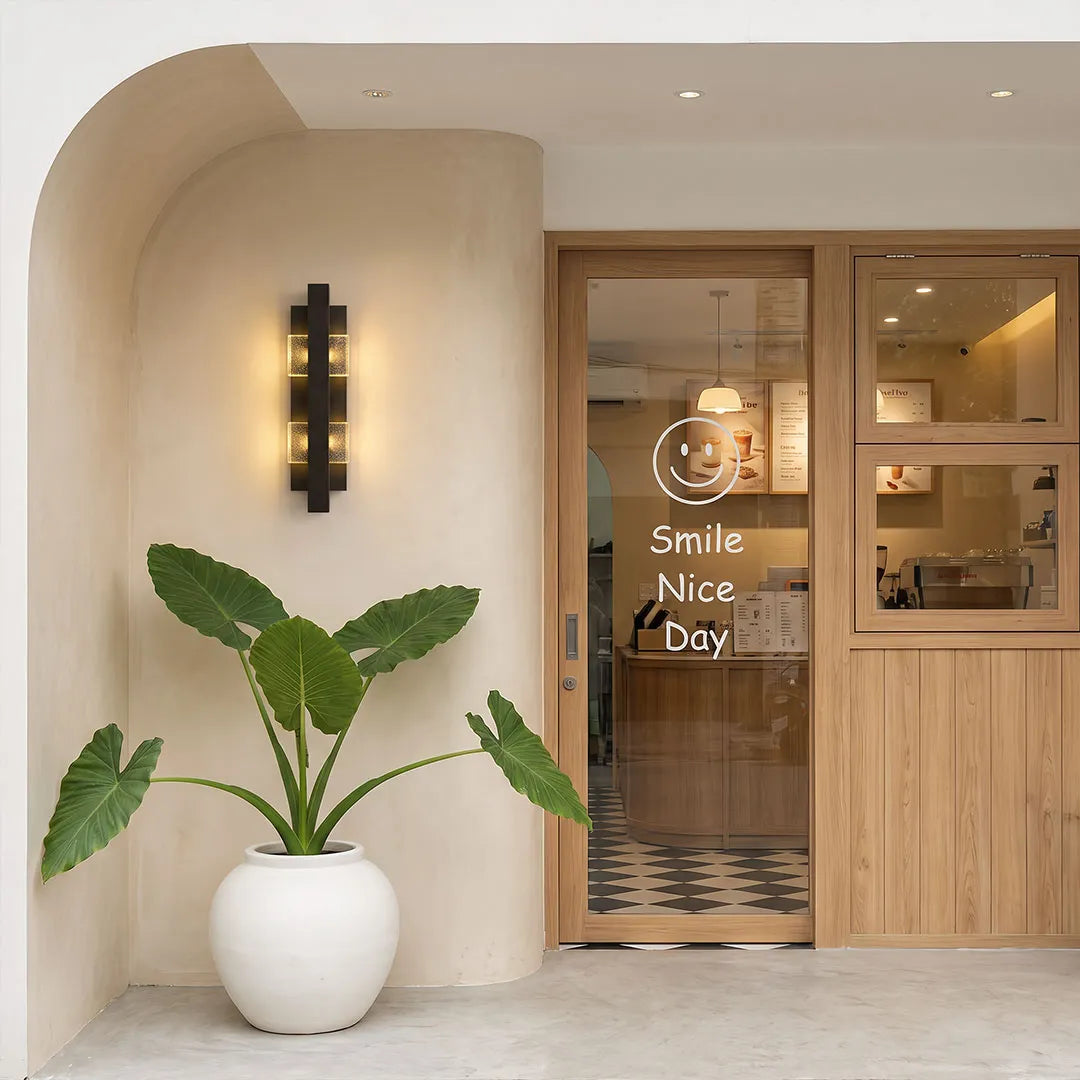 Wall sconce up and down light mounted vertically beside a wooden entry door in a modern interior-exterior transition space.