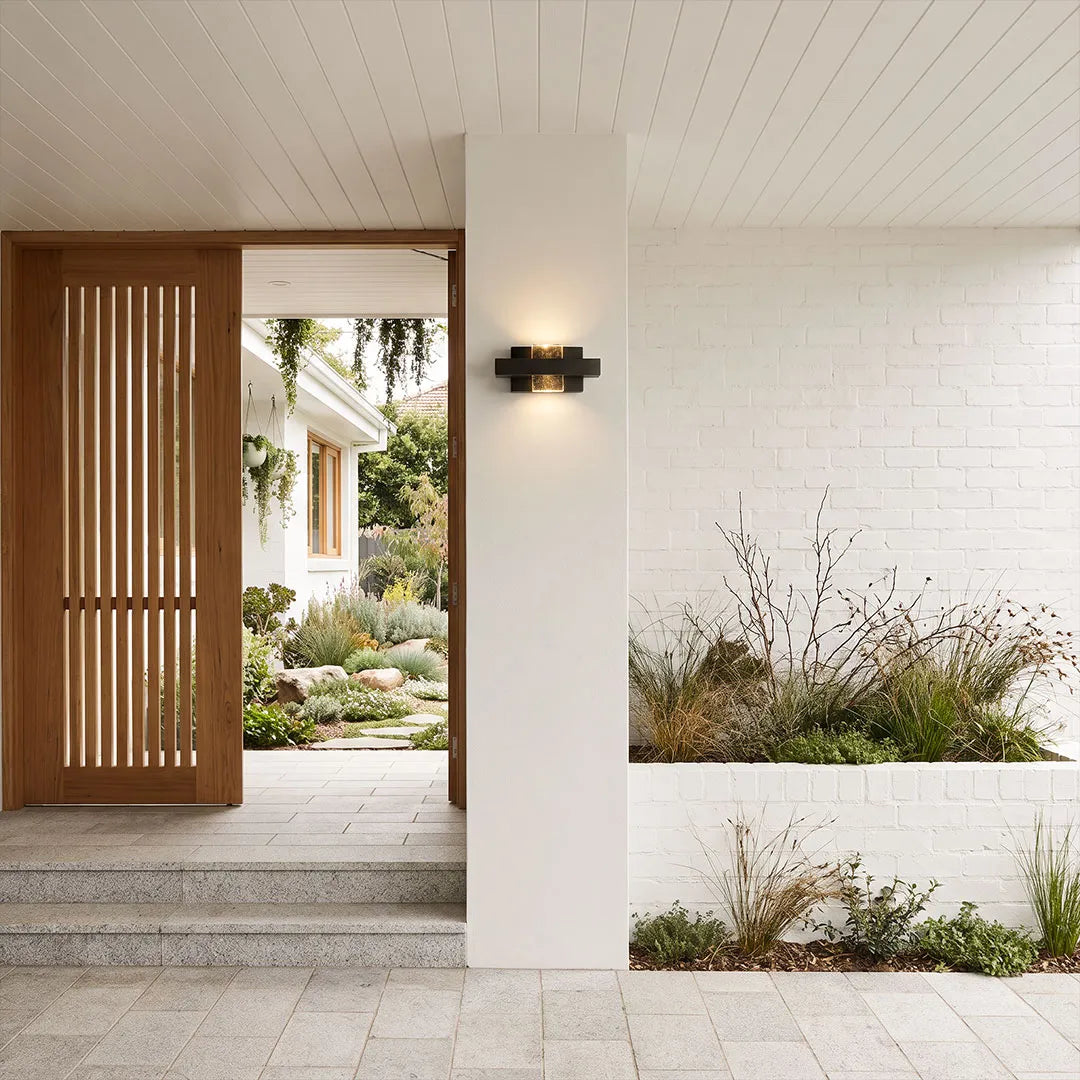 Wall sconce up and down light installed horizontally beside a minimalist front entry porch.