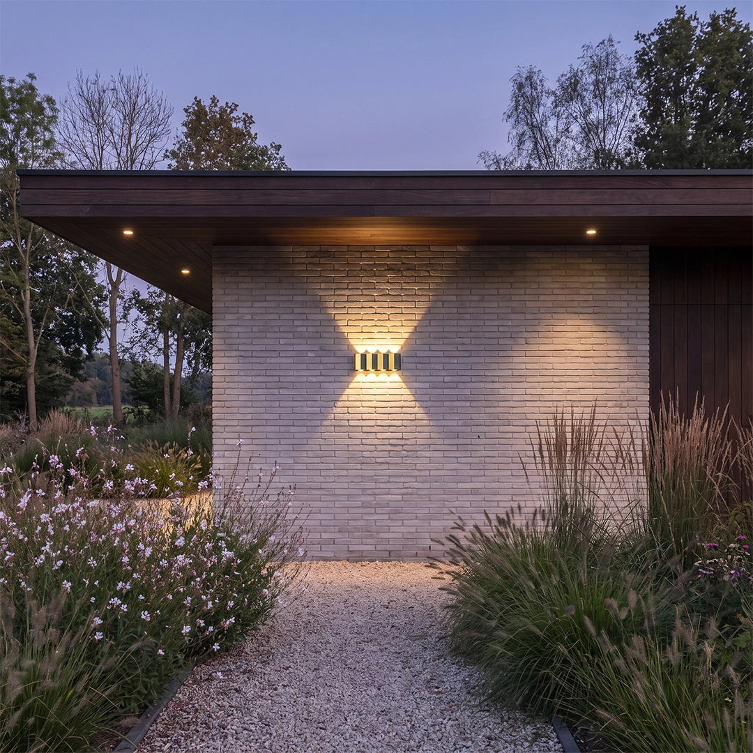 Wall sconce up-down light mounted on a modern exterior wall, creating a wide warm light pattern.