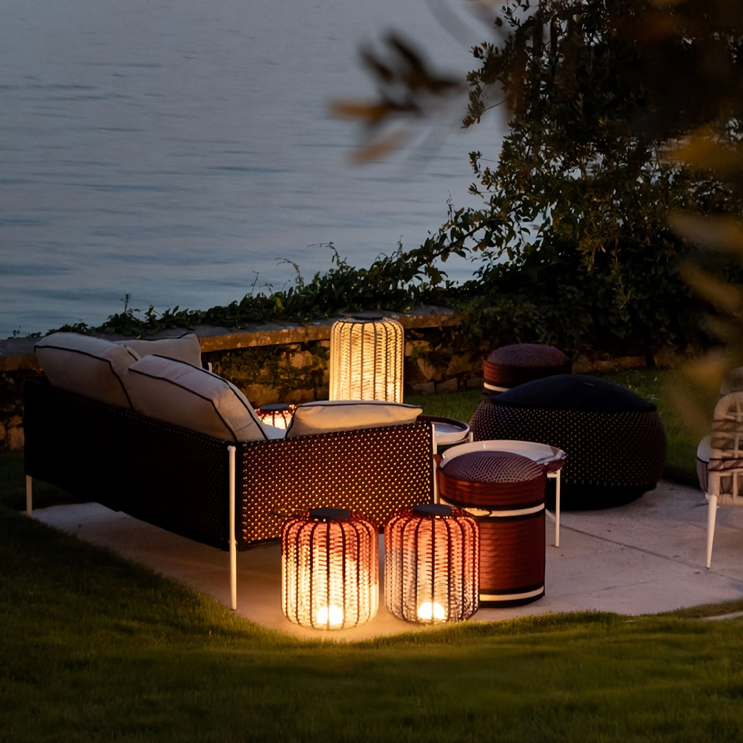 Low and tall outdoor LED lantern lights casting a warm, atmospheric glow near a water feature and modern outdoor sofa at dusk.