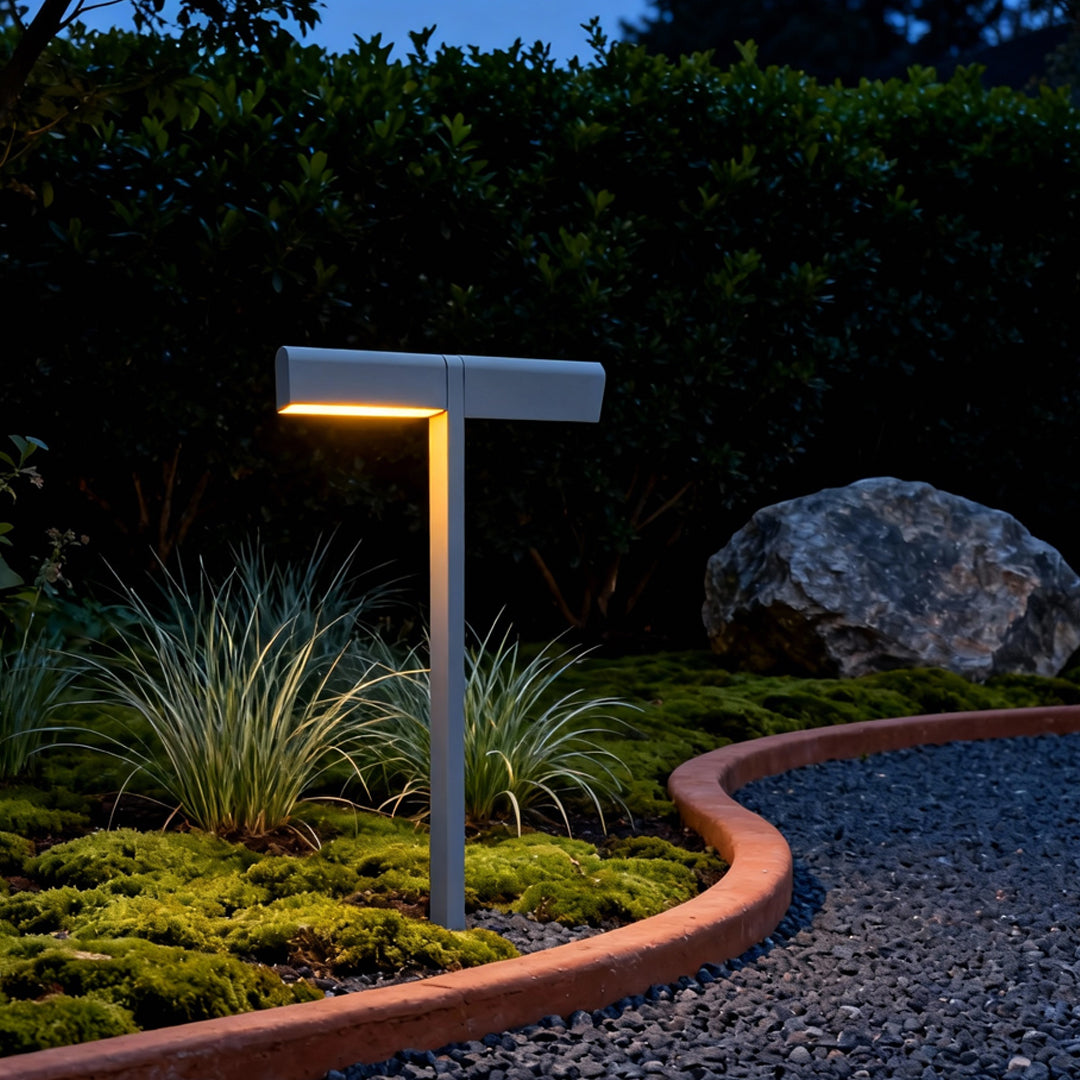 Single T-shaped garden stake glowing warmly along a curved gravel border, enhancing outdoor led pathway lighting ambiance.