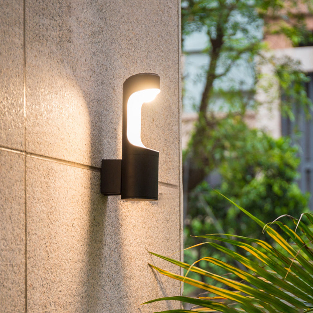 Outdoor wall sconce lighting fixtures mounted on a textured wall beside plants, glowing warmly.