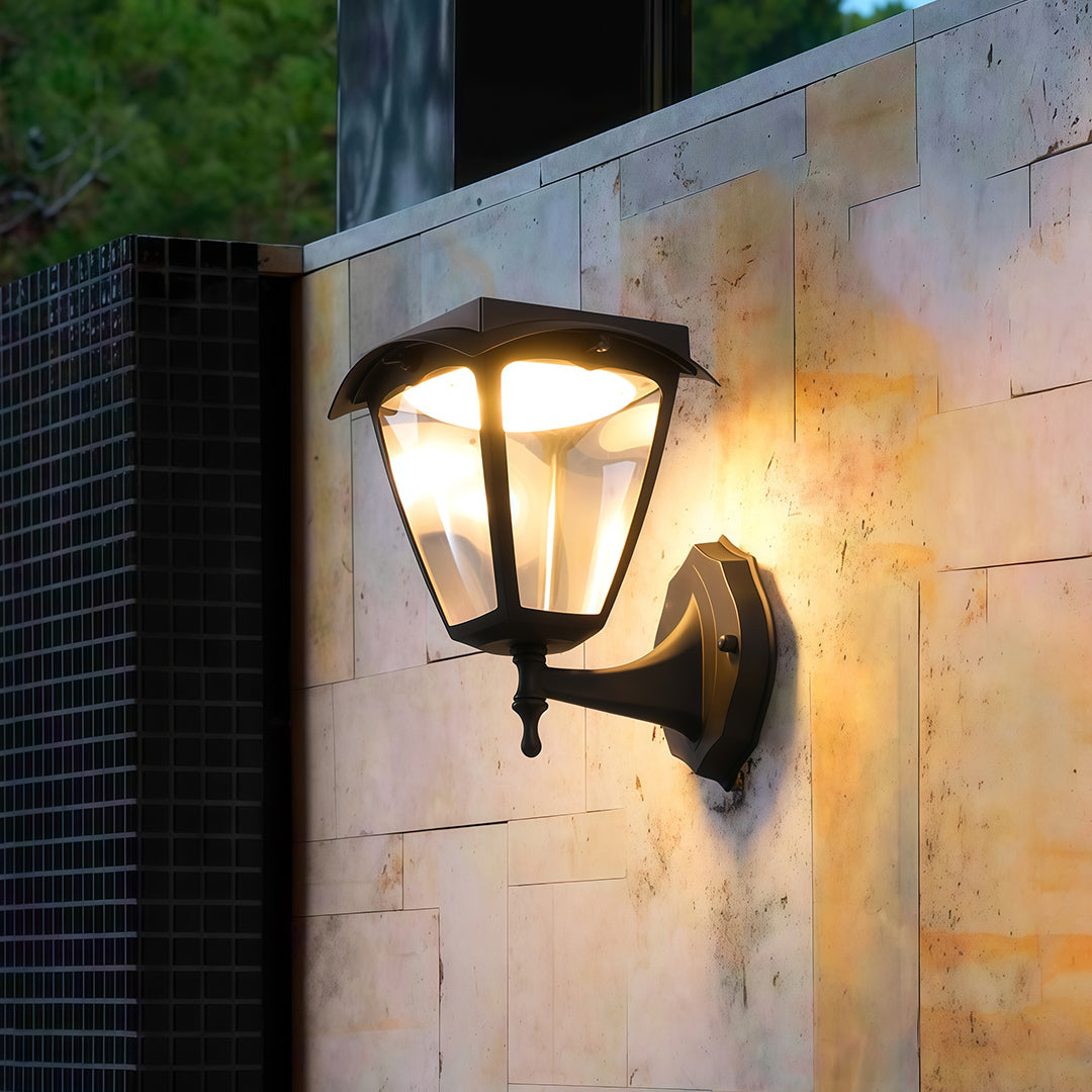 Warm, inviting glow from a single outdoor wall lighting black sconce mounted on a rough stone pillar at night.