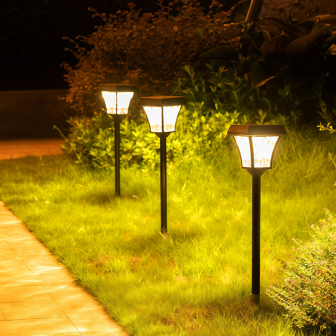 Warm-glowing outdoor solar path lighting fixtures lining a grassy lawn and garden bed at night.