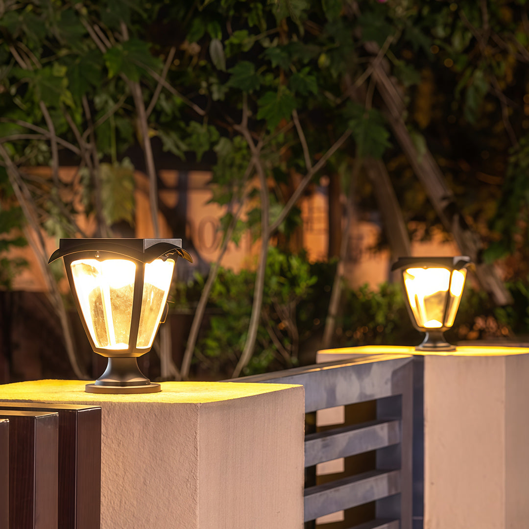 Warm-glowing solar light pillar fixtures in a classic lantern style, illuminating a modern fence at night.
