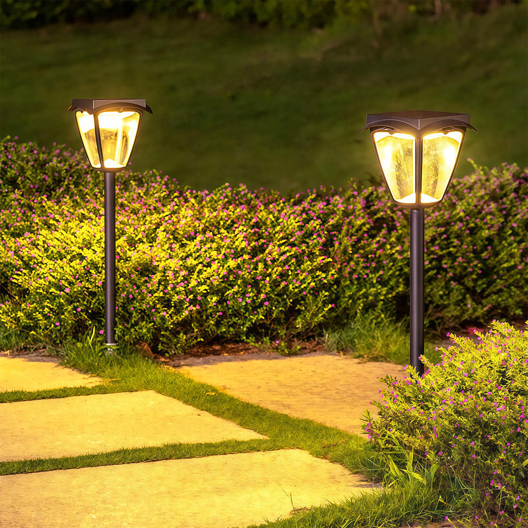 Warm-glowing solar powered path lighting fixtures in a classic lantern style, lining a stone walkway.