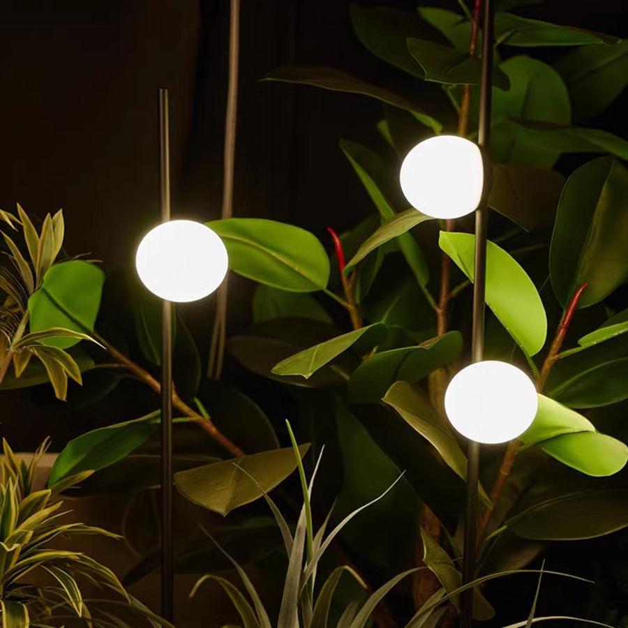 Warm LED orb lights positioned among green plants creating cozy outdoor living space