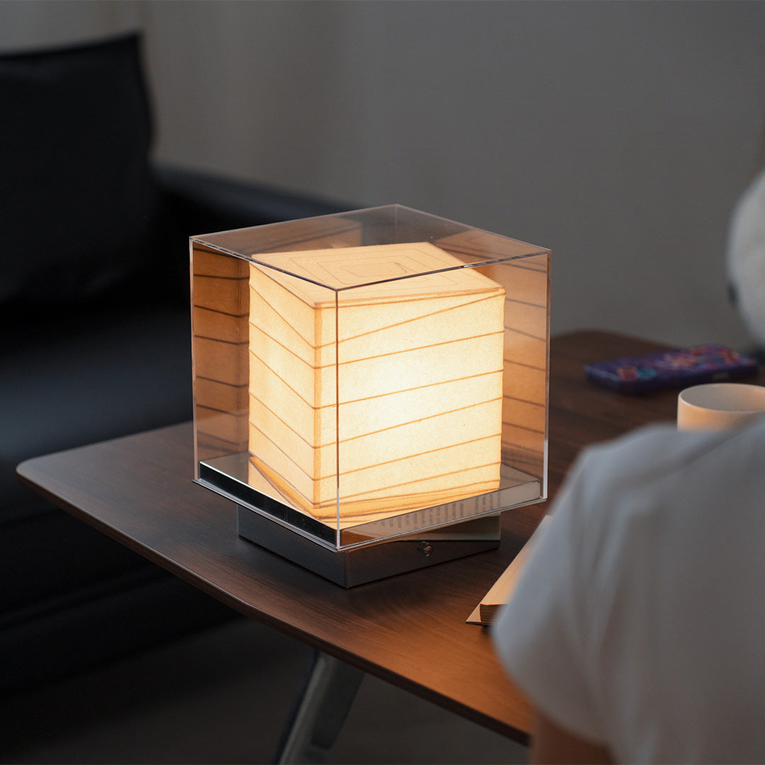 Warm-lit Japanese paper table lamp placed on wooden desk, creating serene ambiance.