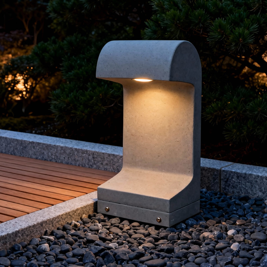 Warm landscape led lighting illuminating a concrete and gravel pathway using a modern curved-top outdoor bollard fixture.