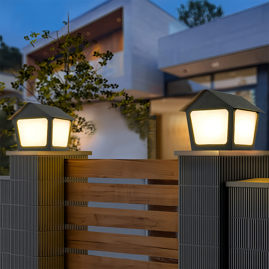 Warm-toned deck post cap lights installed on pillars flanking a wooden gate, offering clear entry illumination at night.