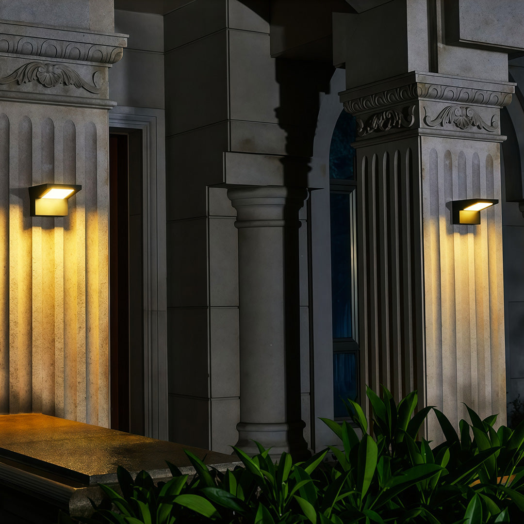 Warm wall mount outdoor light fixtures illuminating large classical columns at an entryway.