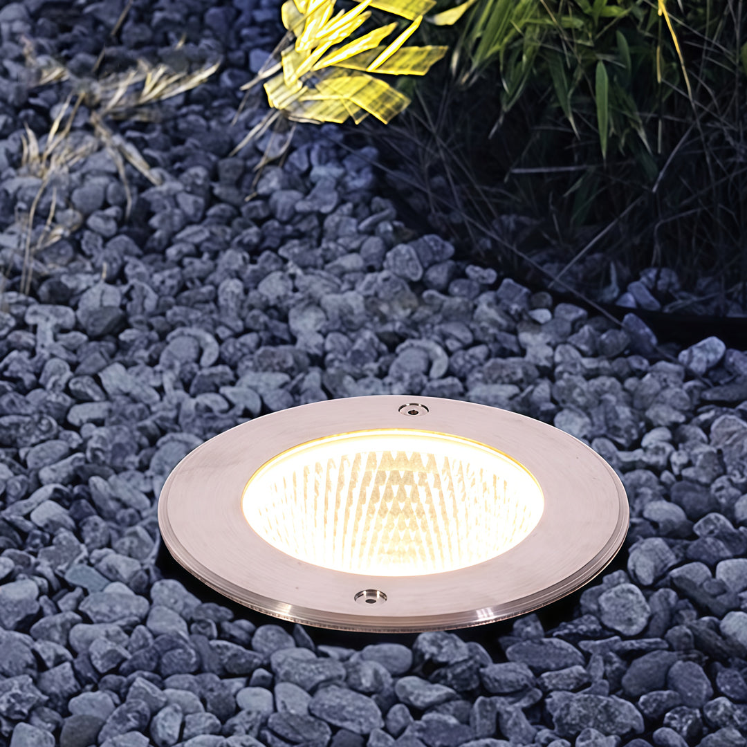 Warm white inground light installed in decorative gravel for soft landscape accent lighting.