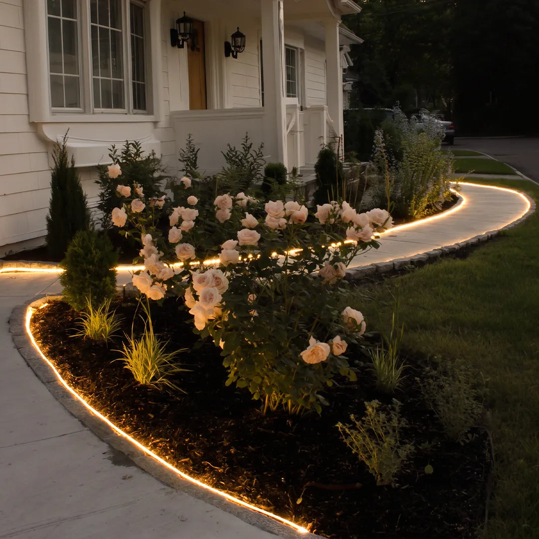 Waterproof LED light strips outlining a curved garden border, creating continuous warm accent lighting around flowers and shrubs.