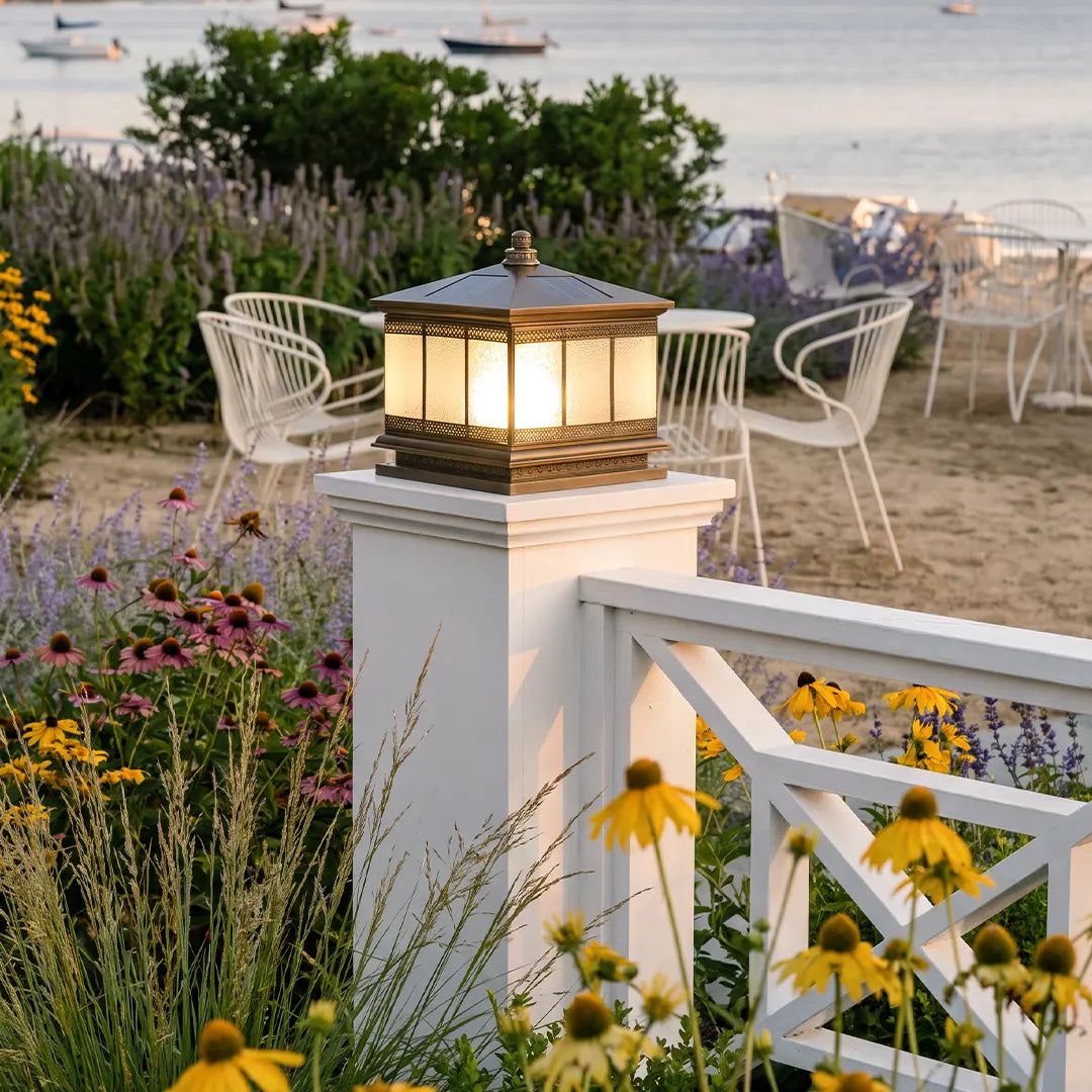 Waterproof outdoor gate pillar light installed on a white fence post near a garden patio by the water.