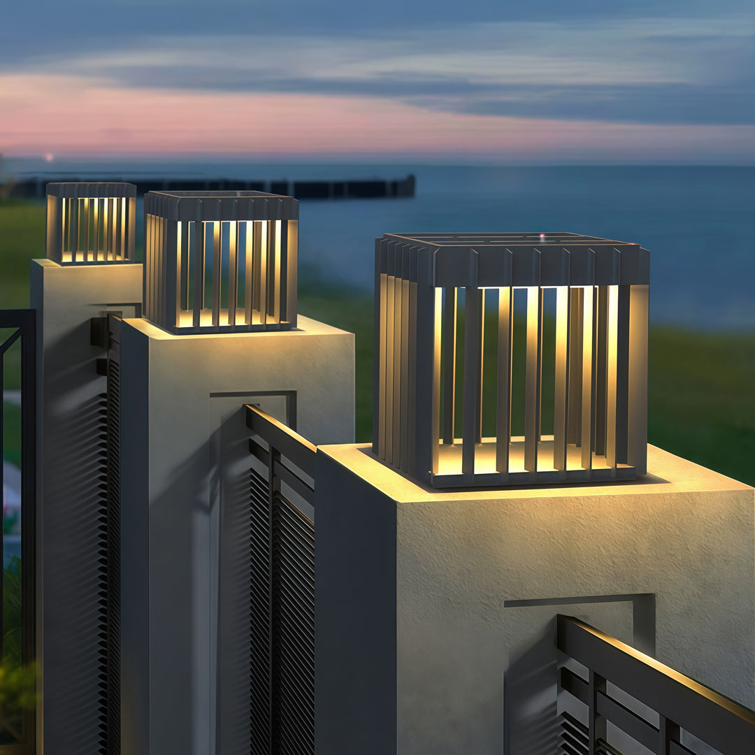 A close-up view of a waterproof outdoor pillar light on a modern outdoor platform, highlighting its warm glow and vertical-bar design.