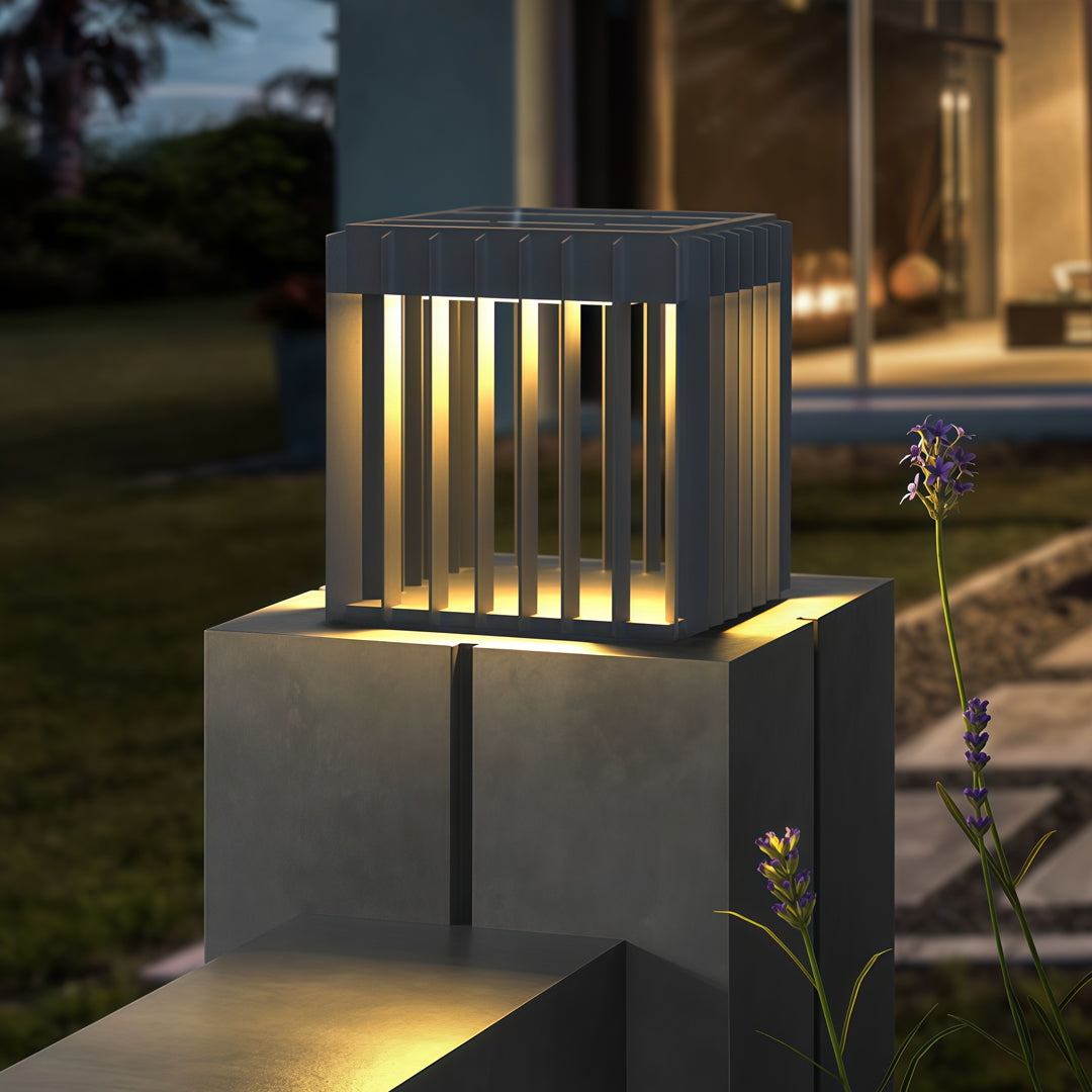 A waterproof outdoor pillar light placed on a stone pedestal, radiating warm light in a modern landscaped setting.