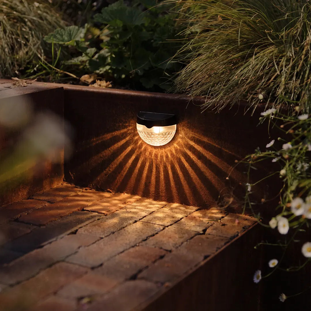 Waterproof solar fence lights installed on a garden retaining wall casting decorative beam patterns at night.