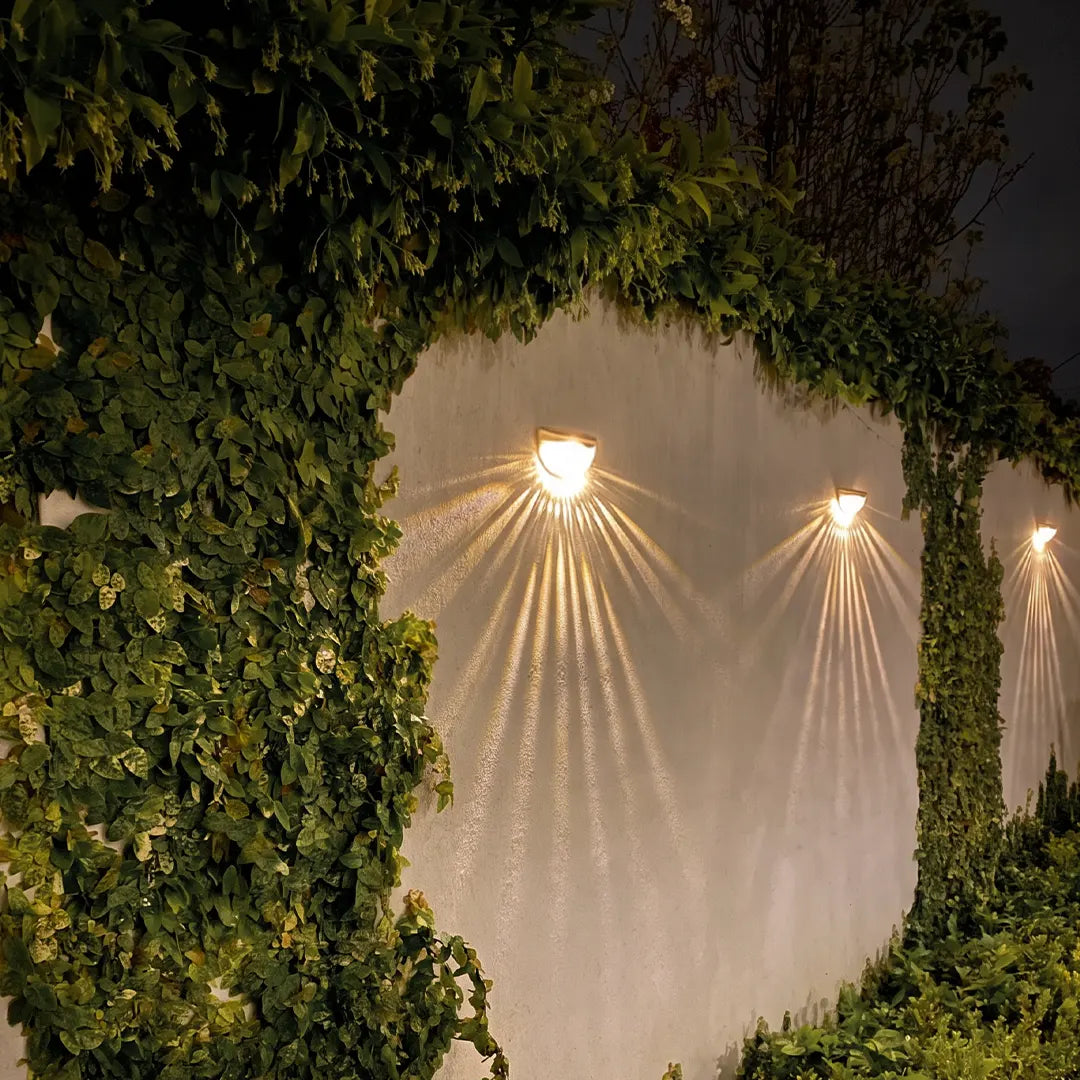 Waterproof solar fence lights attached to an outdoor wall with ivy, creating radiant downward light patterns.