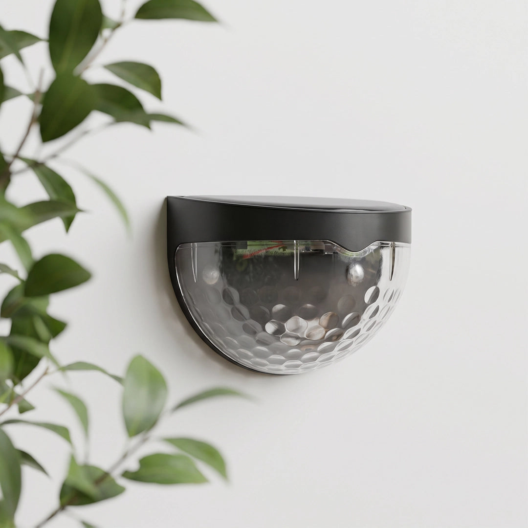 Waterproof solar fence lights with a black top and clear textured shade shown mounted on a white wall.