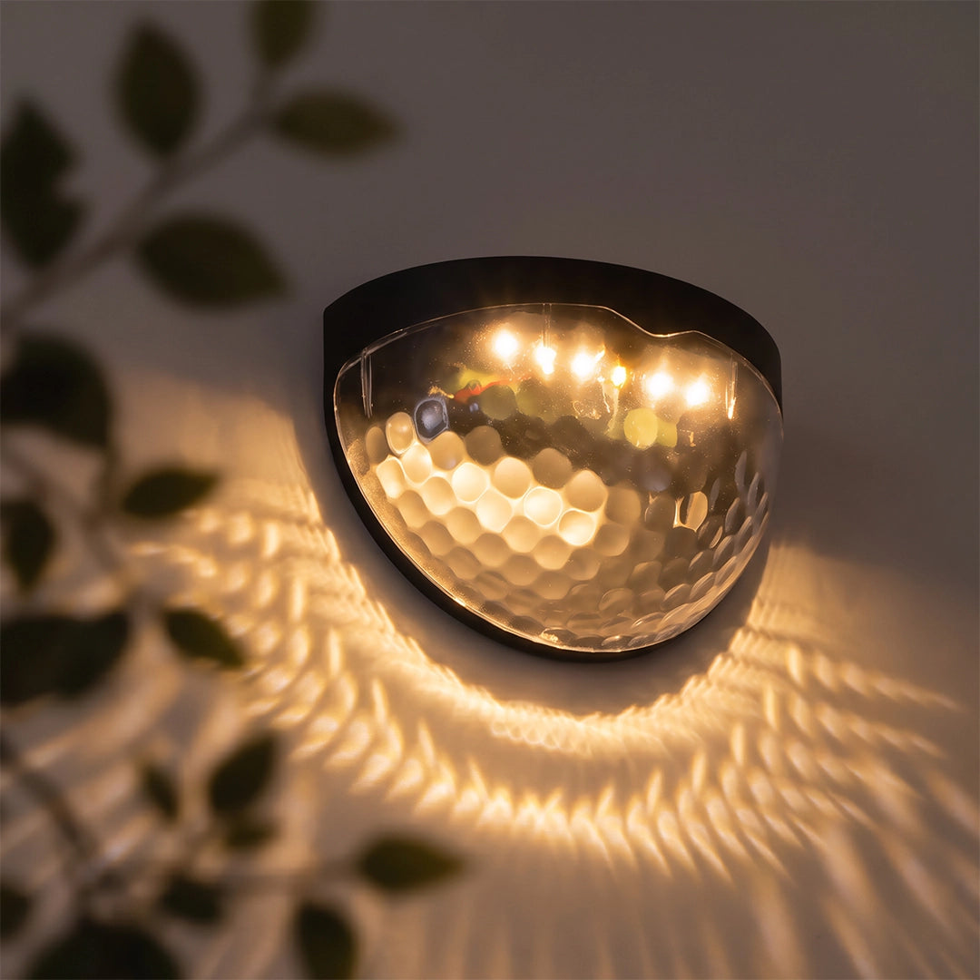 Waterproof solar fence lights mounted on a wall, casting a warm decorative glow pattern at night.