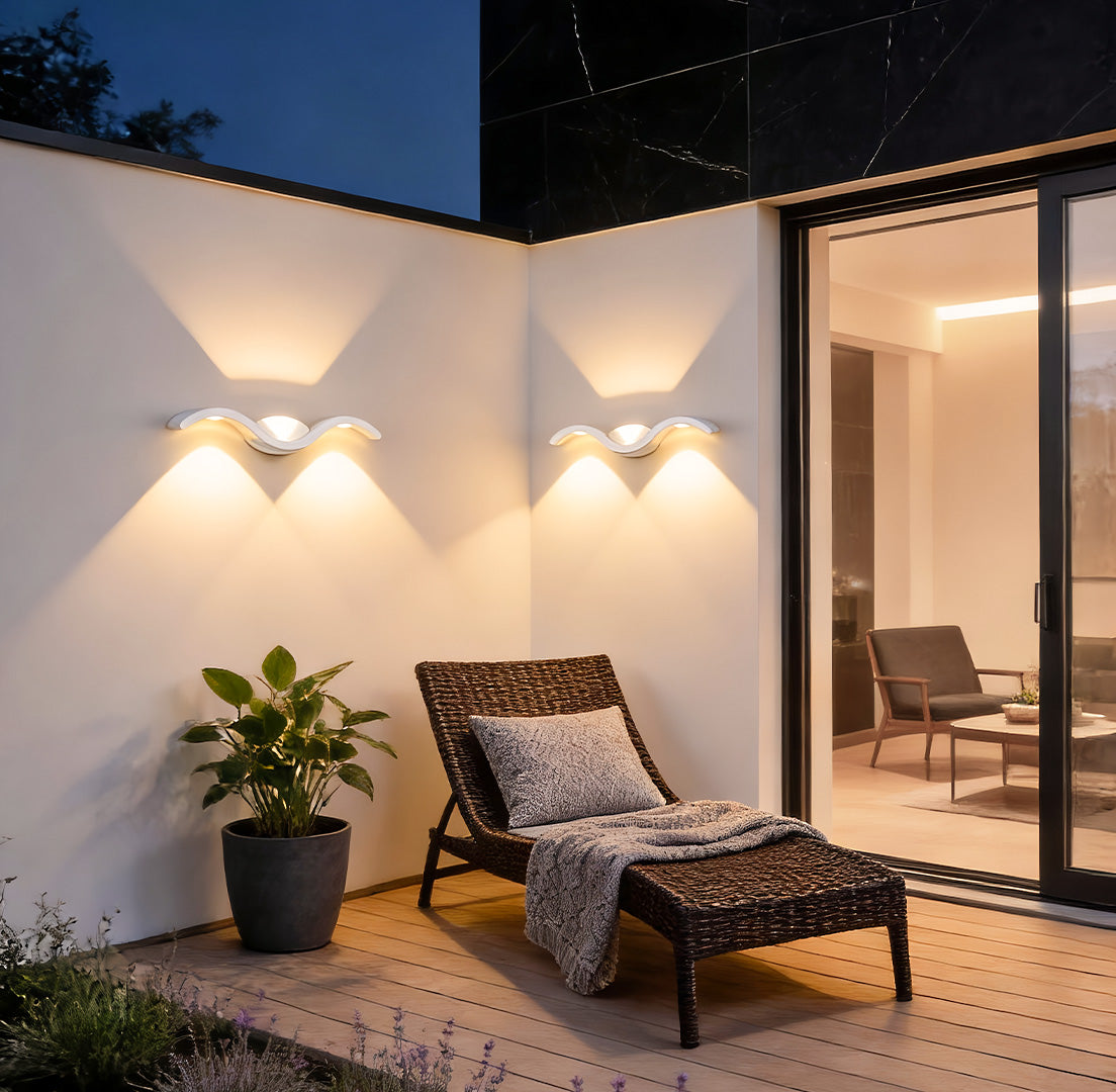 Wave wall sconce mounted on an exterior wall beside lounge chairs, creating warm ambient lighting for a contemporary backyard.