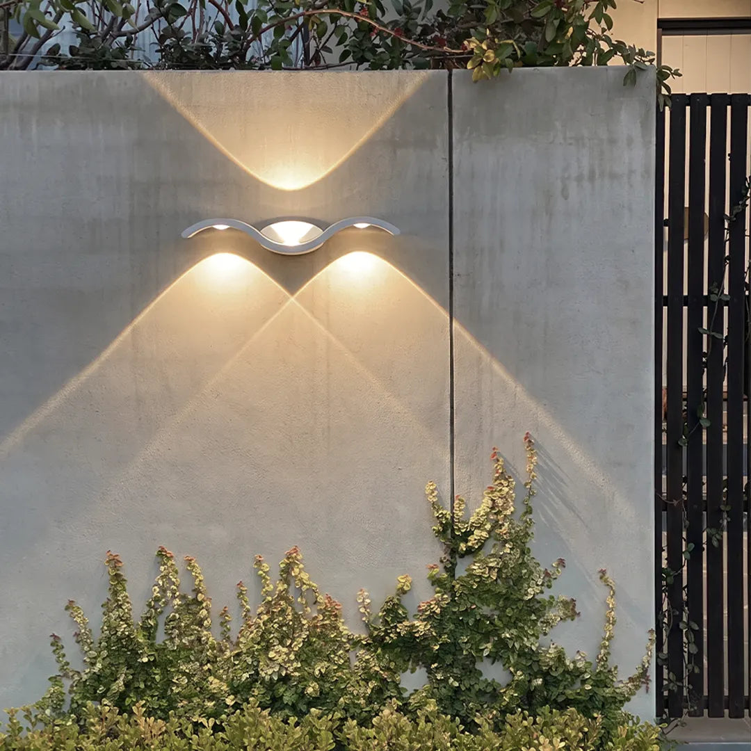 Wave wall sconce mounted on a concrete exterior wall with warm up and down lighting.