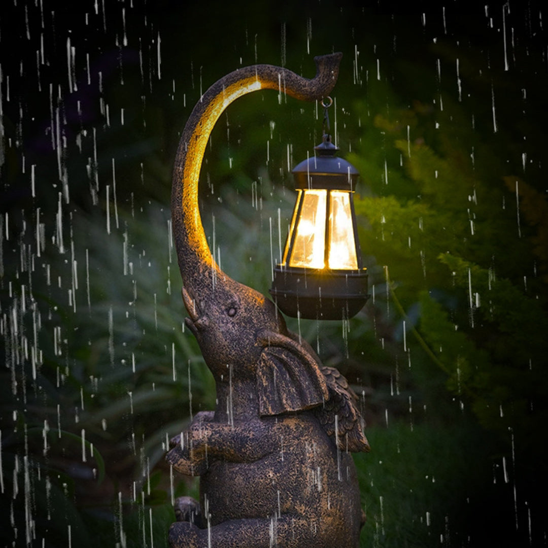 Weather-resistant elephant garden light with glowing lantern shown during rainfall with lighting effect