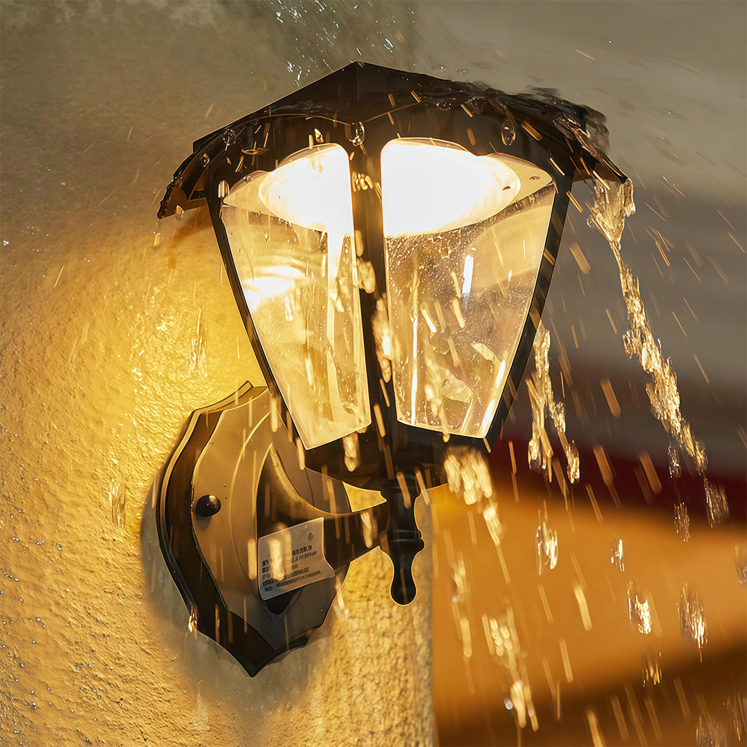 Weatherproof outdoor wall lighting black fixture shining warmly while being sprayed with water.