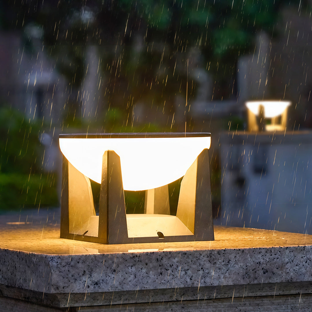 Durable weatherproof solar powered bollard light illuminating a pillar brightly during a rainstorm at night.