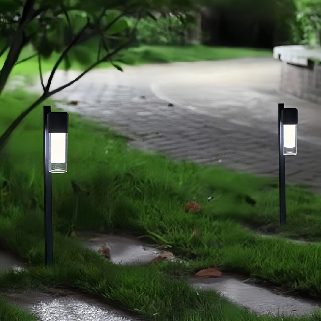 Contemporary path light placed along a wet stone pathway in a lush green outdoor setting.