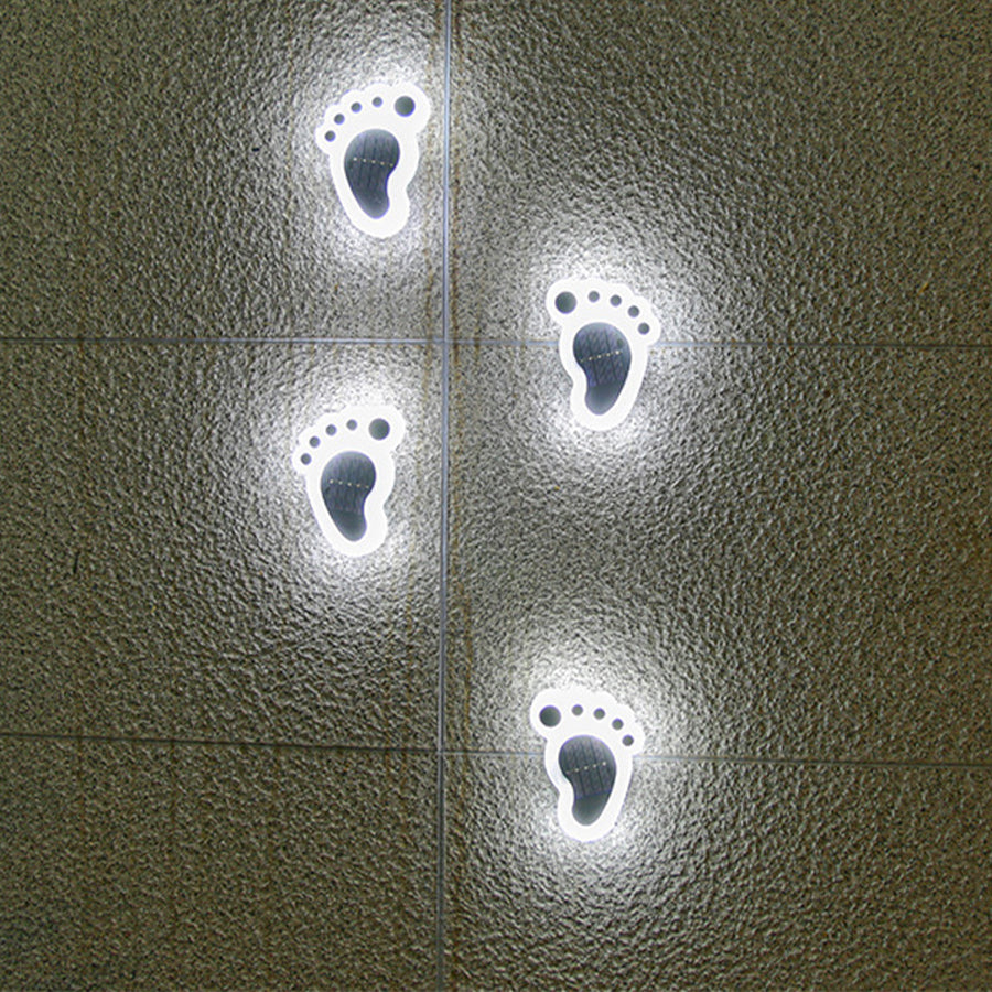 Whimsical footprint solar lights creating playful lighting pattern on concrete walkway surface