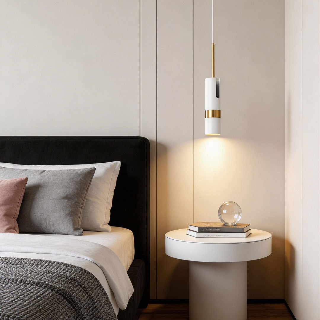 A white adjustable cylindrical pendant light hanging over a modern white bedside table spot.