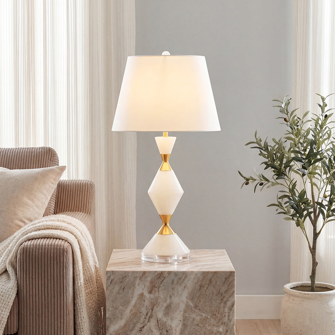 Elegant white contemporary table lamps with gold diamond stone stem on a marble plinth beside sofa.