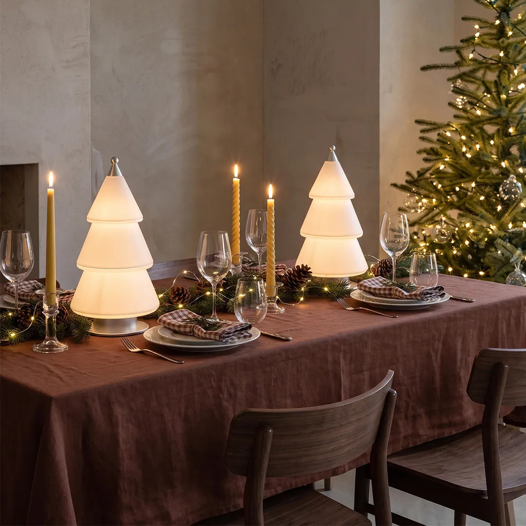 White contemporary table lamps placed on a dining table in a festive holiday setting with candles and a decorated Christmas tree.