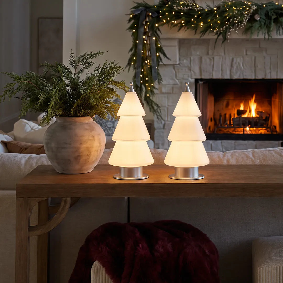 White contemporary table lamp styled on a console table in a cozy holiday living room with a fireplace and festive greenery.