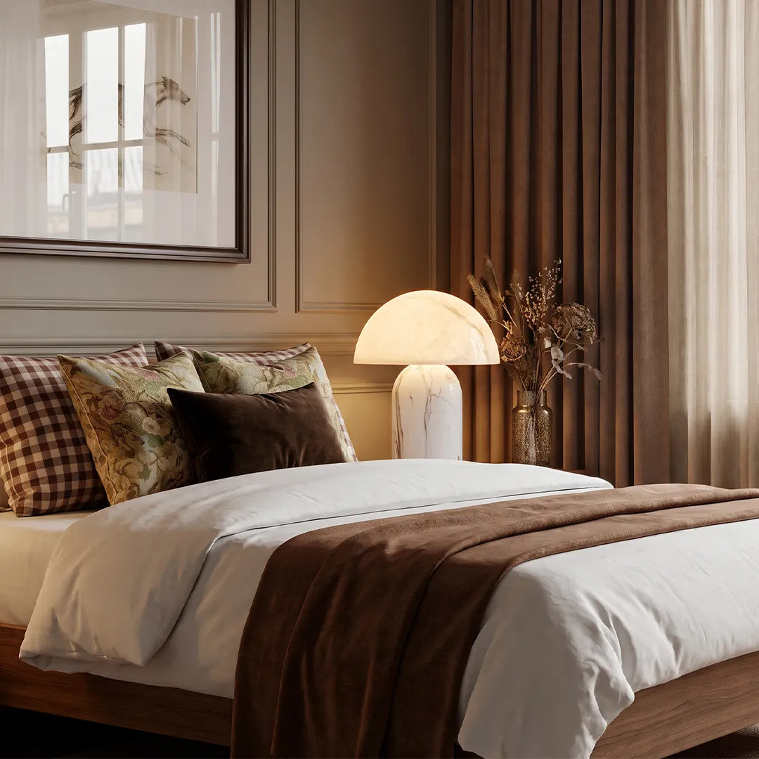 White contemporary table lamps styled on a bedside table in a warm modern bedroom with layered neutral bedding.