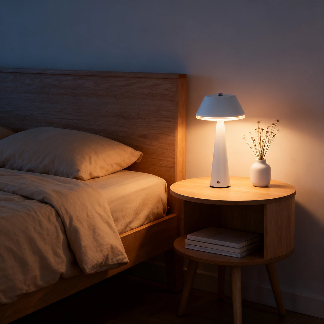 White cordless rechargeable table lamps providing soft ambient light on a wooden bedside nightstand in a cozy bedroom. 