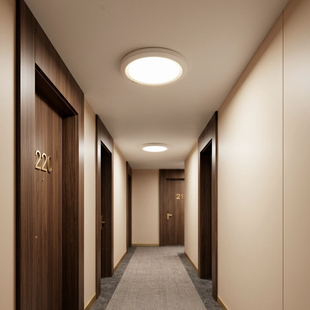 White flush mount ceiling light used in a hotel corridor with soft warm lighting