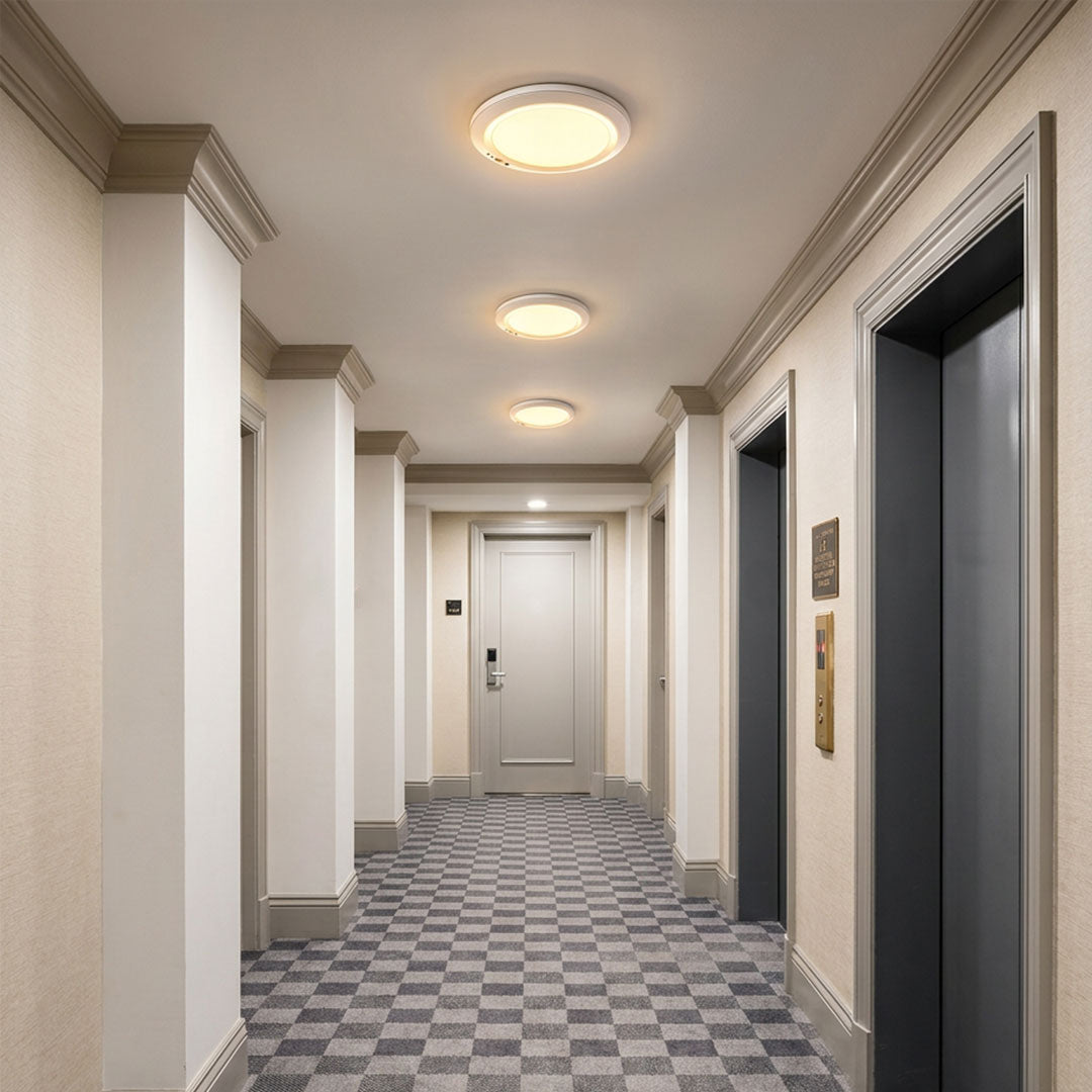 White flush mount ceiling light installed in a modern apartment hallway with warm illumination
