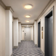 White flush mount ceiling light installed in a modern apartment hallway with warm illumination
