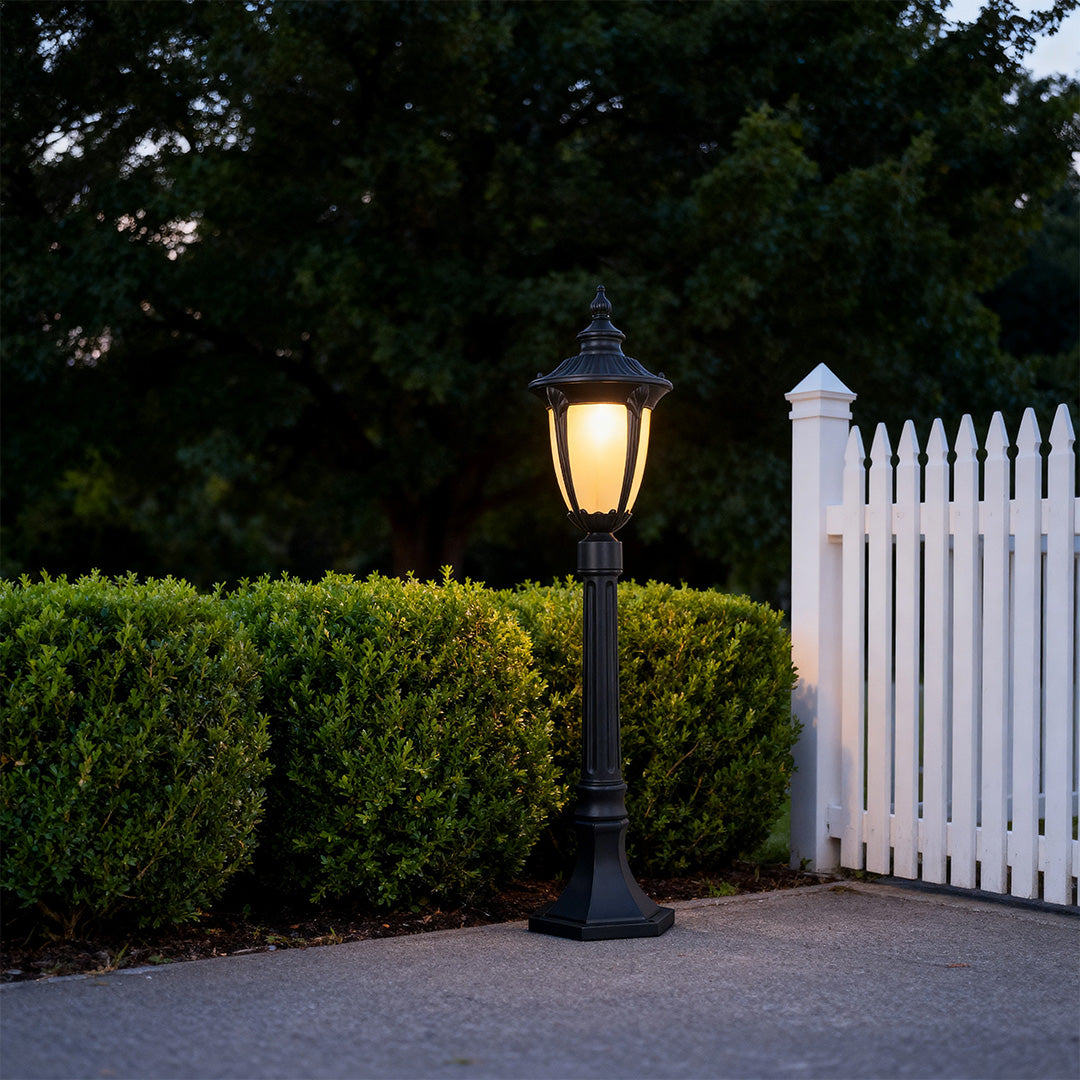 Bollard light for garden beside a white gate, stylish and warm outdoor lighting solution
