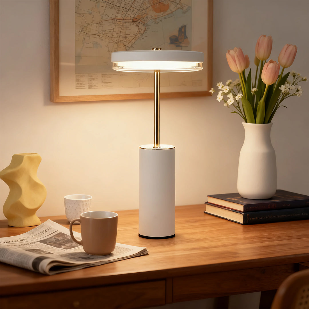 White and gold cylinder table lamps illuminating a wooden desk with flowers and a map backdrop.