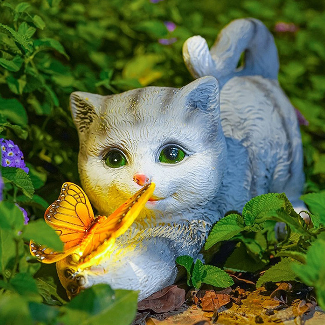 White and gray kitten garden ornament holding glowing butterfly among green foliage