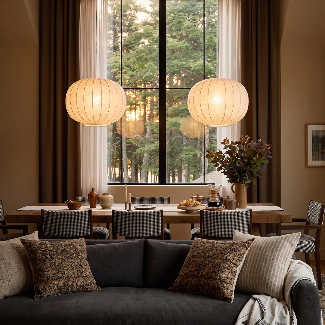 White modern chandelier hanging above a cozy dining and living area, featuring two round white shades and warm ambient lighting.